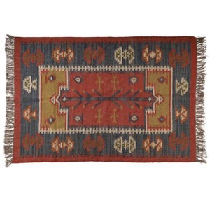 May include: Rectangular area rug with a geometric pattern. The rug features a central red field with a detailed design in gold, blue, and white. The border is a dark blue with repeating motifs. The rug has fringed edges.