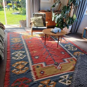 May include: A vibrant, rectangular area rug with a central red field and intricate geometric patterns in blue, gold, and white. The rug is placed in a living room setting, adding a touch of warmth and color to the space.