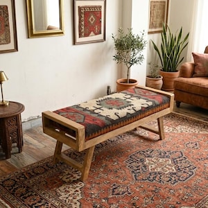 May include: A wooden bench with a rectangular seat featuring a patterned rug design in red, beige, and gray. The bench is in a room with a patterned rug, a brown sofa, and framed artwork on the wall.