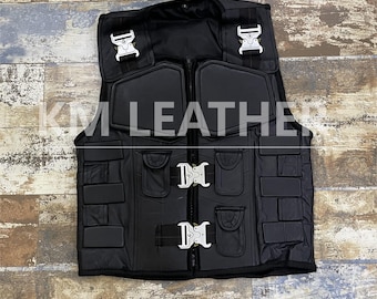 Puede incluir: Chaleco táctico de cuero negro con múltiples bolsillos y hebillas plateadas. El chaleco tiene un diseño acolchado y el texto "KM LEATHER" está impreso en la parte delantera.
