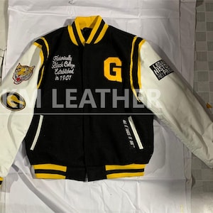 Könnte beinhalten: Schwarz-gelbe Collegejacke mit weißen Ärmeln. Mit dem Buchstaben "G" und dem Text "Historically Black College Established in 1901". Enthält einen Tiger-Aufnäher und den Text "ALL OF THIS IS OURS".