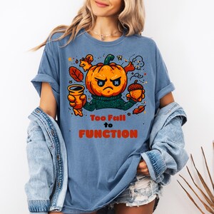 Puede incluir: Camiseta azul con un diseño de calabaza enfadada con un jersey verde. El texto "Too Full to Function" está impreso en naranja. Diseño temático de otoño.