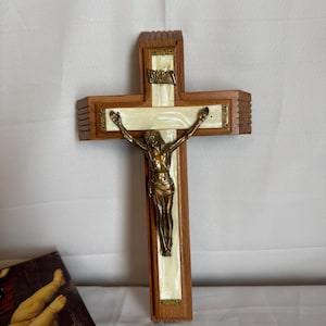 May include: Wooden crucifix with a bronze figure of Jesus. The cross has a light brown wood frame with a white and gold inlay. The figure is detailed with outstretched arms. The text "INRI" is visible at the top.