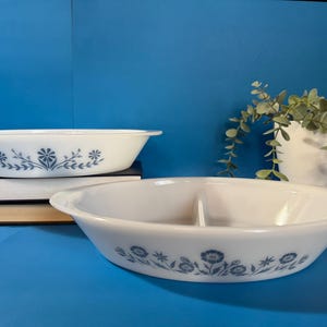 Könnte beinhalten: Zwei ovale Servierschalen in Weiß mit blauen Blumenmustern. Eine Schale ist in zwei Abschnitte unterteilt. Die Schalen stehen auf einer blauen Oberfläche, mit Büchern und einer Topfpflanze im Hintergrund.