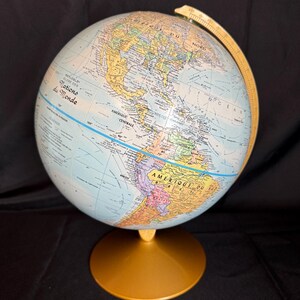 Może przedstawiać: Szczegółowy globus z podstawą i łukiem południka w kolorze złotym. Globus przedstawia jasnoniebieski ocean i kolorowe kontynenty z tekstem w języku francuskim. Globus jest ustawiony na czarnym tle.