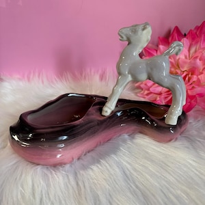 Peut inclure: Un pot de fleurs vintage en céramique avec une figurine de cerf. Le pot a un design en deux parties avec un dégradé de rose à noir. Le cerf est gris clair avec des accents blancs. Une pièce décorative pour la décoration intérieure.