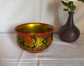 May include: A decorative, hand-painted wooden bowl with a red exterior, gold interior, and floral design in black and gold. A small, brown vase holds a white rose. The bowl is approximately 4 inches in diameter.