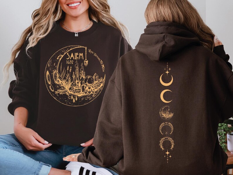 a woman wearing a black sweatshirt with a gold design on the front, which includes a moon and stars, and a back design with a series of crescent moons and stars.