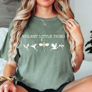 A woman with long, wavy blonde hair wearing a green t-shirt with a graphic design and text printed on it.