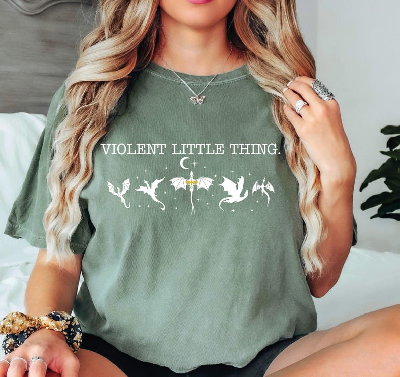 A woman with long, wavy blonde hair wearing a green t-shirt with a graphic design and text printed on it.