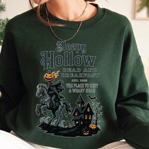 A green sweatshirt with a Halloween-themed graphic design featuring a spooky horse, a castle, and jack-o-lanterns.