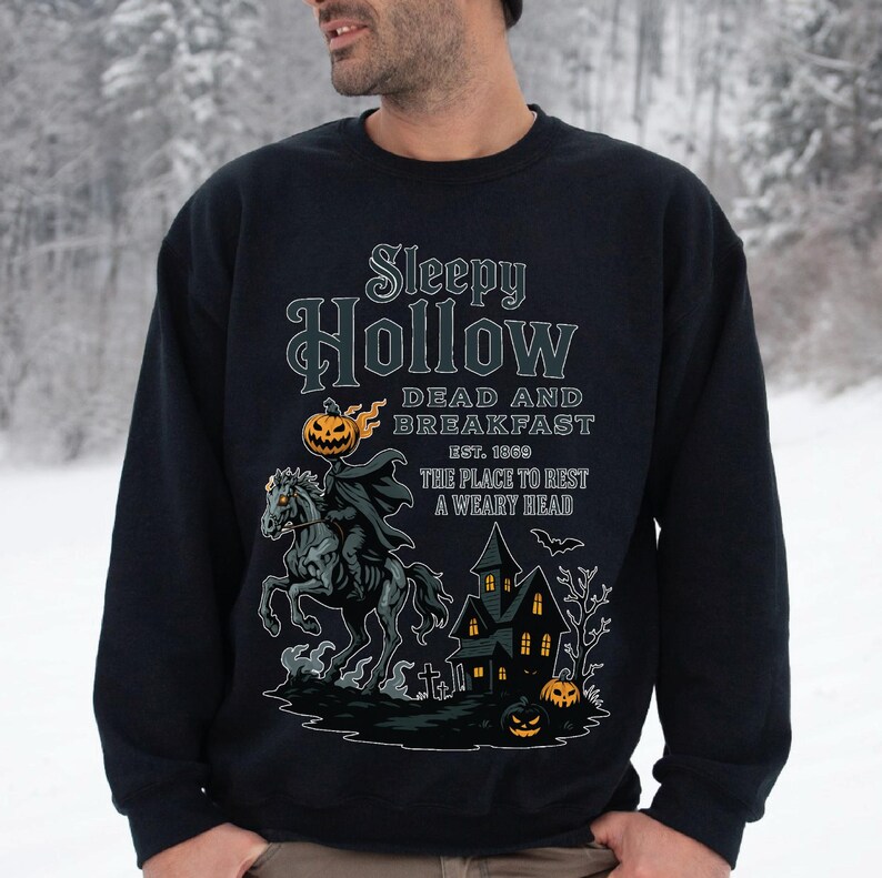 A man wearing a black sweatshirt with a Halloween-themed design, including a skeleton riding a horse, a castle, and jack-o-lanterns.