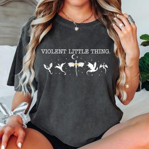 A woman wearing a black t-shirt with a graphic design of a dragon and the text "VIOLENT LITTLE THING" printed on it.