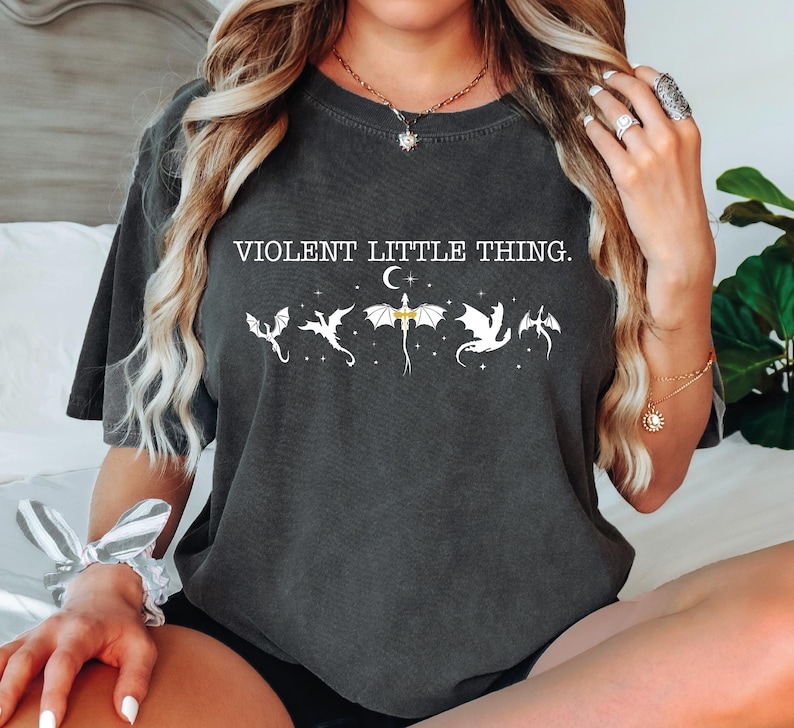 A woman wearing a black t-shirt with a graphic design of a dragon and the text "VIOLENT LITTLE THING" printed on it.