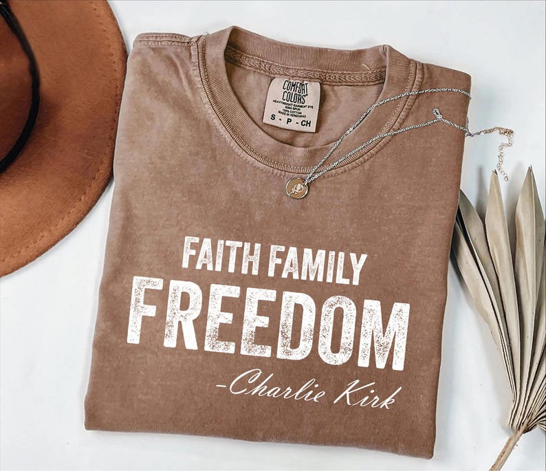 A brown t-shirt with the text "Faith Family Freedom" printed on it, along with a necklace and a hat.