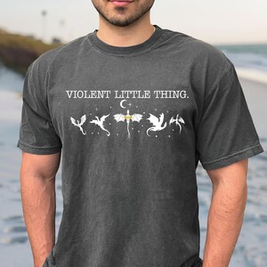 A man wearing a gray t-shirt with the text "VIOLENT LITTLE THING" printed on it.