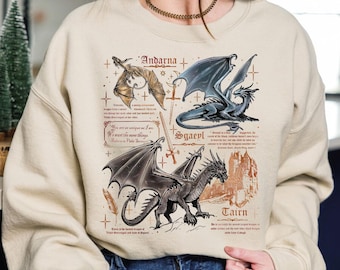 May include: A beige sweatshirt featuring three dragon illustrations with text. The dragons are in shades of brown, gray, and blue. The text includes dragon names and quotes. The sweatshirt has a crew neck and long sleeves.