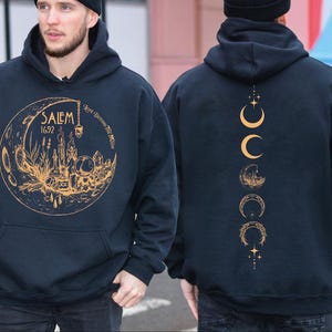 A man wearing a black hoodie with a gold design on the front and back.