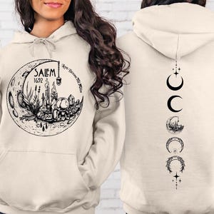 A woman wearing a white hoodie with a graphic design on the front and a back featuring a series of black symbols and images.