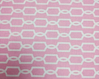 May include: Pink fabric with a repeating white geometric chain pattern. The design features interconnected, elongated hexagons linked by oval shapes, creating a textured, symmetrical design. The fabric has a soft, matte finish.