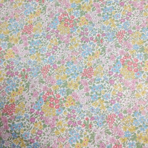 May include: A close-up of a floral fabric with a dense pattern of small flowers in shades of pink, yellow, blue, and green on a white background. The flowers are tightly packed together, creating a vibrant and colorful design.