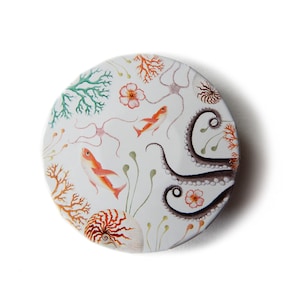 May include: A round, white ceramic button with a colorful illustration of an octopus, fish, coral, and flowers. The button is perfect for adding a touch of whimsy to any project.