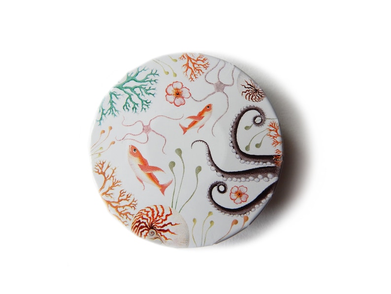 May include: A round, white ceramic button with a colorful illustration of an octopus, fish, coral, and flowers. The button is perfect for adding a touch of whimsy to any project.