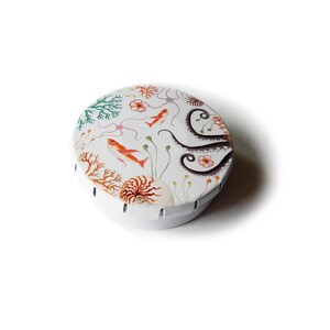 May include: A round, white metal tin with a colorful design of an octopus, seahorse, and coral. The tin is perfect for storing small items like jewelry, buttons, or coins.