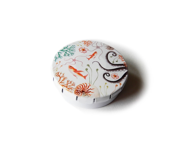 May include: A round, white metal tin with a colorful design of an octopus, seahorse, and coral. The tin is perfect for storing small items like jewelry, buttons, or coins.