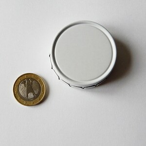 May include: A white metal lid with a slightly raised edge. The lid is round and has a smooth surface.