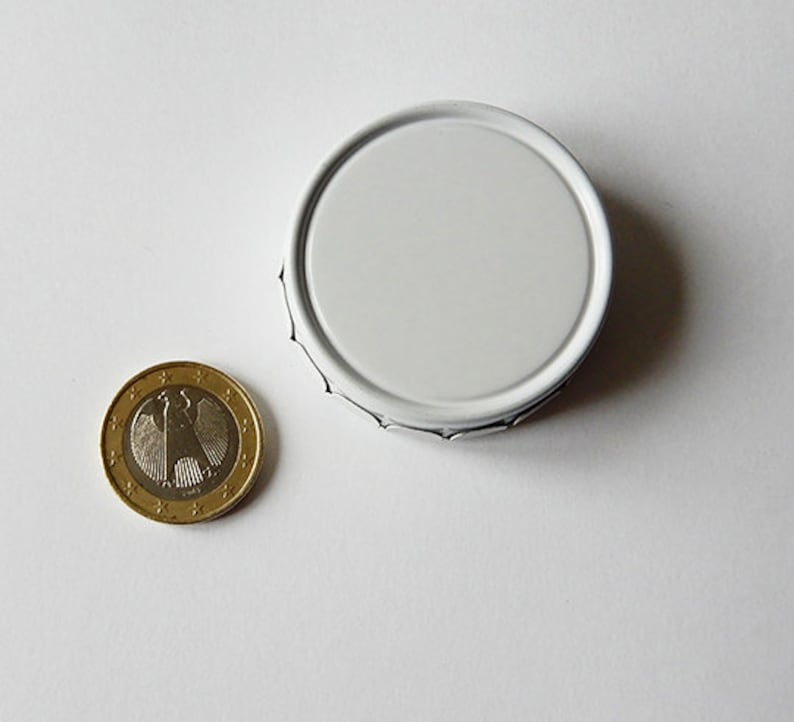 May include: A white metal lid with a slightly raised edge. The lid is round and has a smooth surface.