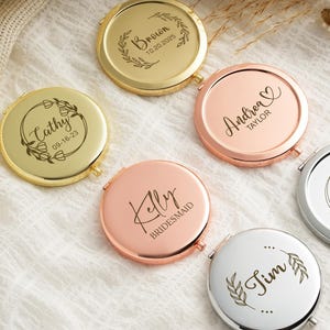 Puede incluir: Varios espejos compactos personalizados en oro, oro rosa y plata. Cada espejo presenta texto y fechas personalizadas, con diseños de coronas florales. Los espejos están dispuestos sobre una superficie blanca texturizada, ideales para regalos.