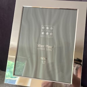 May include: Silver-plated brass photo frame, 8 x 10 inches, with a reflective, polished surface. The frame has a wide border and features the text "SIXTREES London + New York" and "Reframo".