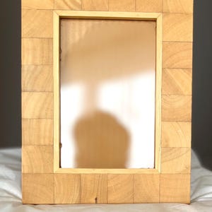 Op de afbeelding: Een rechthoekige fotolijst opgebouwd uit lichtgekleurde houten blokken in een rasterpatroon. De lijst heeft een gladde, dunne binnenrand rondom een centrale rechthoekige opening, met een afwerking die de natuurlijke houtnerf laat zien.