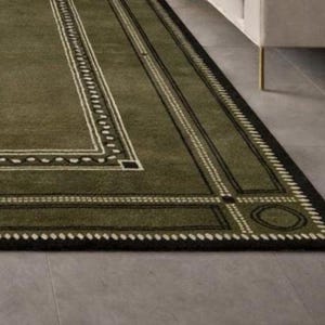 Olive green modern area rug with geometric border design placed in a minimalist living room with beige sofa and natural light