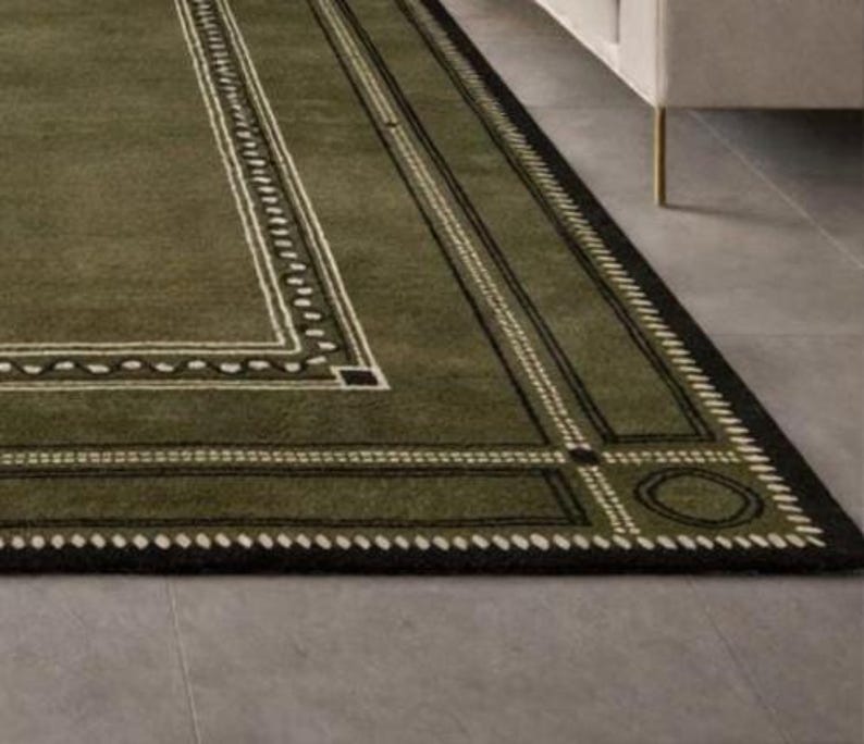 Olive green modern area rug with geometric border design placed in a minimalist living room with beige sofa and natural light