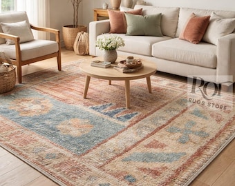 Puede incluir: Salón con una gran alfombra de aspecto envejecido. La alfombra tiene una sección central azul con motivos florales, bordeada por secciones beige y óxido. La habitación incluye un sofá beige, sillas de madera y una mesa de centro redonda.