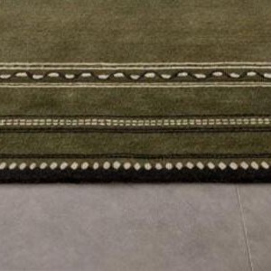 Olive green modern area rug with geometric border design placed in a minimalist living room with beige sofa and natural light
