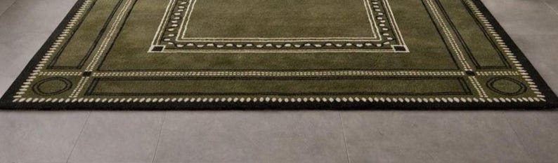 Olive green modern area rug with geometric border design placed in a minimalist living room with beige sofa and natural light