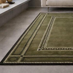 Olive green modern area rug with geometric border design placed in a minimalist living room with beige sofa and natural light