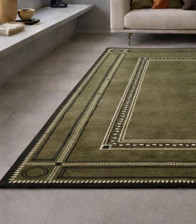 Olive green modern area rug with geometric border design placed in a minimalist living room with beige sofa and natural light