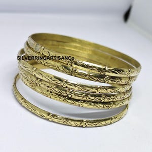 Peut inclure: Plusieurs bracelets dorés avec un motif floral et de feuilles en relief. Les bracelets sont empilés sur une surface blanche. Le texte "SILVERRINGARTISANCO" est visible sur l'image.