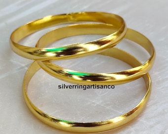 May include: Three gold-coloured bangles are intertwined, reflecting light. The smooth, rounded bands are stacked, creating a layered effect. The image includes the text "silverringartisanco".