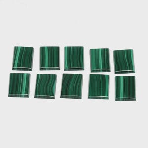 May include: Ten square-cut malachite gemstones with a polished finish. The stones display a vibrant green color with dark green, wavy banding patterns. Each stone has a silver-colored edge.