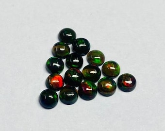 May include: A collection of polished, round gemstones, mainly dark green with flashes of red and gold. The gemstones are arranged in a triangular shape against a white background. The stones have a smooth, reflective surface.