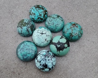 May include: Eight turquoise-coloured, round stones with varying shades of blue-green and dark veining. The stones are arranged in a circular pattern on a grey surface. Each stone has unique patterns.
