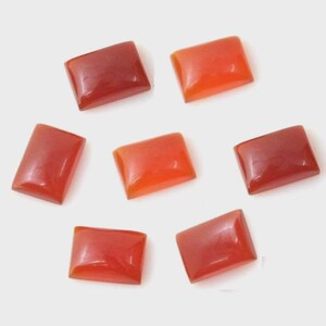 Puede incluir: Siete gemas rectangulares en tonos rojos y naranjas están dispuestas sobre una superficie blanca. Las piedras tienen un aspecto pulido y brillante, con variaciones en la intensidad del color. Las gemas son probablemente para la fabricación de joyas.