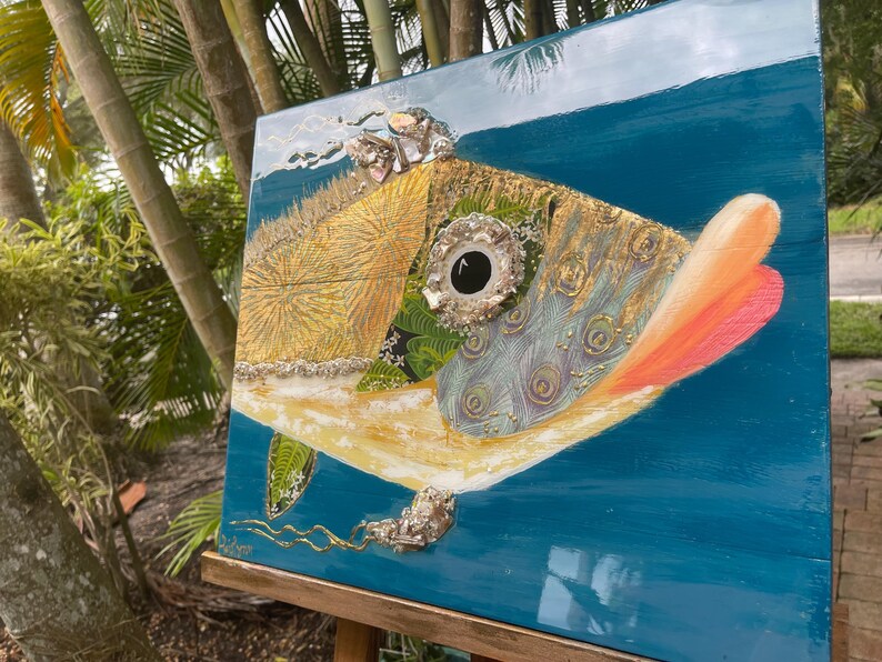 Puede incluir: Una pintura abstracta colorida de un pez con un ojo grande y redondo. El pez est&aacute; pintado en tonos dorados, verdes, azules y naranjas. El fondo es de un azul profundo.