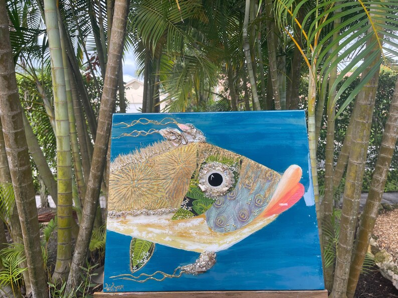 Puede incluir: Una pintura abstracta colorida de un pez con un fondo azul. El pez est&aacute; hecho de diferentes materiales y texturas, incluyendo oro, verde y azul. El ojo del pez es negro y blanco.