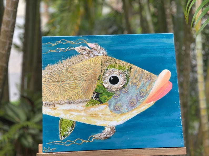 Puede incluir: Una pintura colorida y mixta de un pez con un cuerpo azul, verde y dorado. El pez tiene un ojo grande y redondo y una boca rosa. El fondo es de un azul vibrante.